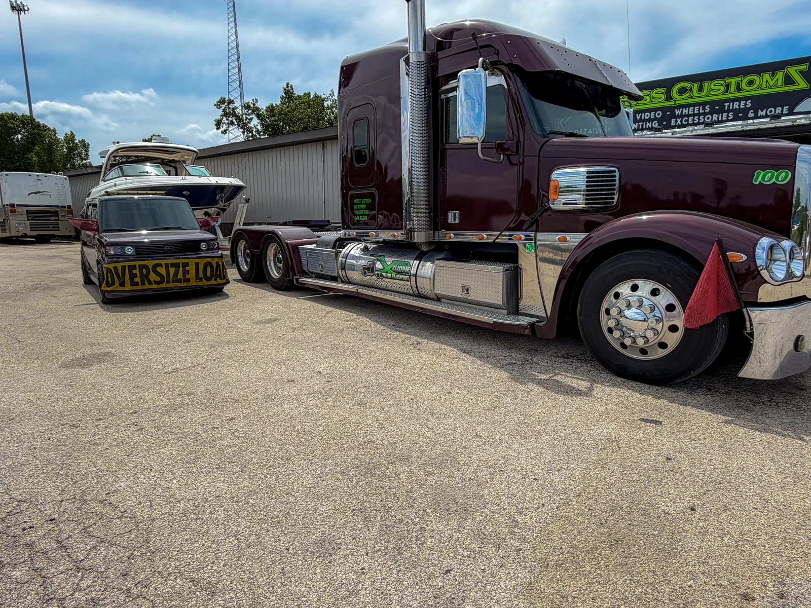 Pilot car with its OVERSIZE LOAD banner parked nose-on beside the Xclusive Transport Freightliner Coronado