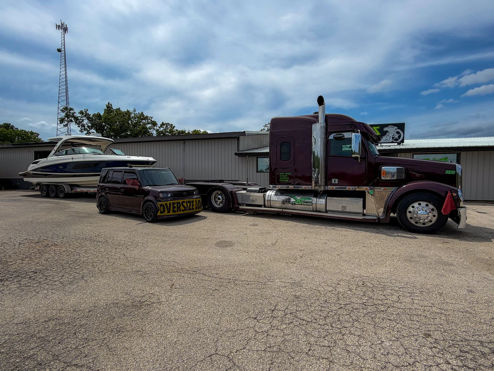 Xclusive Transport pilot car with an OVERSIZE LOAD banner beside the Freightliner Coronado and a boat on the trailer